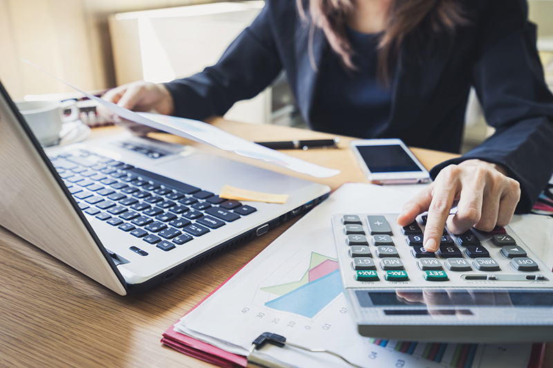 Closeup of person at laptop using a calculator looking at paperwork